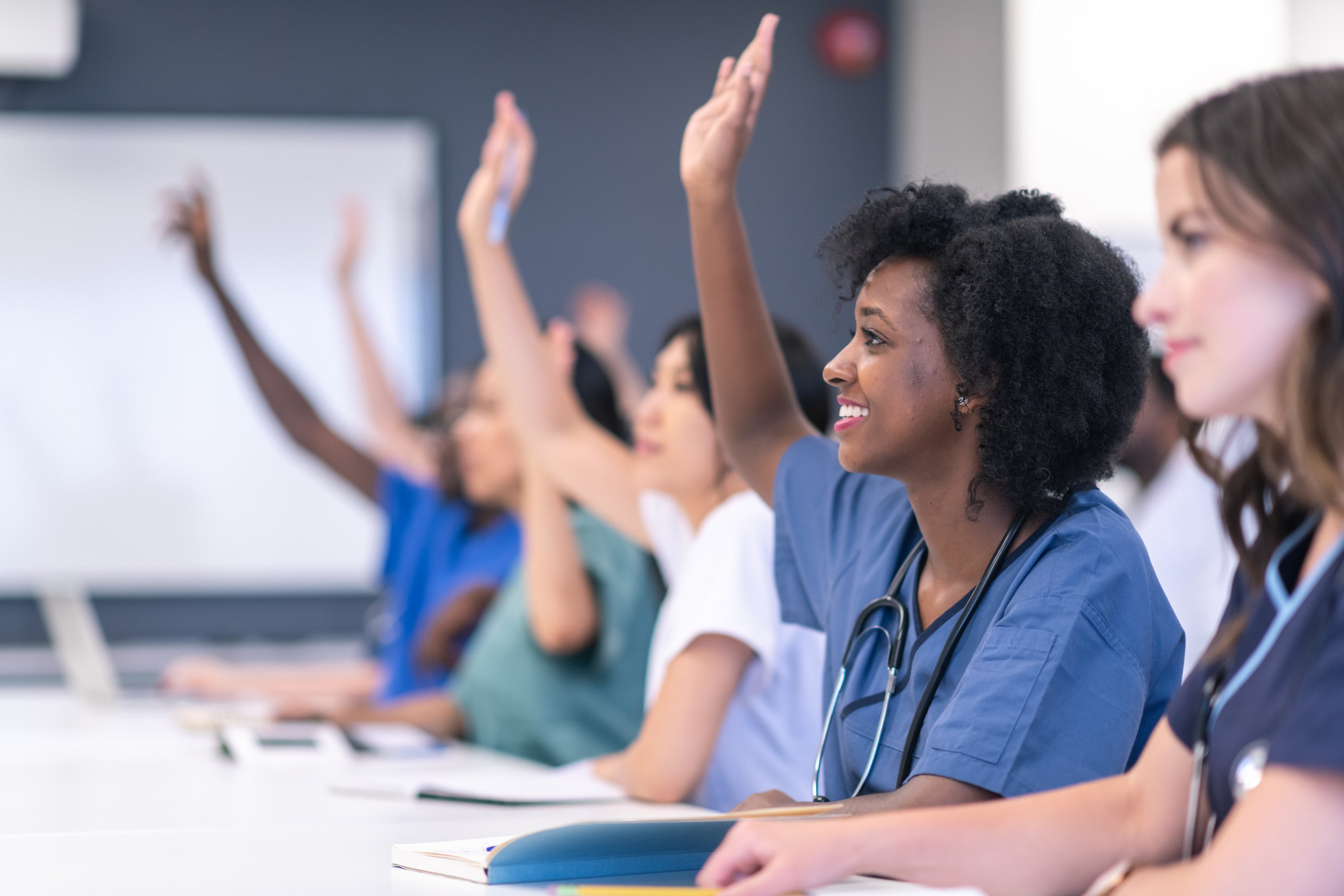Students in medical training class raise hands in lecture